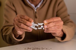 Unrecognizable elderly man, out of focus, with a handful of cigarettes in his hands, which he has split in half, rejecting tobacco.
