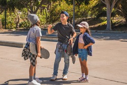Three Caucasian skating children, dressed in casual and urban clothes, greet each other happily after meeting in a skate park.