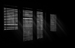Beams of sunlight through old wooden blinds. Light coming through windows of an old abandoned house. Abstract background, black and white image. 