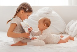 sister explaining and reading baby in bed a book