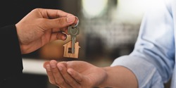 Cropped image Hands of real estate agent offering/giving a house key to smart man in blue shirt while standing together over modern bank as background. Broker/Seller/Dealer concept.