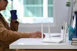 Closeup view of a wireless router with young man using laptop computer in background.