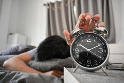 Young man lying on bed and turning off an alarm clock in the morning.