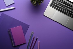 Flat lay computer laptop, potted plant and stationery on purple background.
