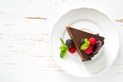 Chocolate cake with raspberry, blackberry, mint, white plate, white wood background, top view