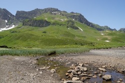 Mountain brook or stream opening into a dried up lake. There is very little  water in the brook and the lake bottom is exposed because there is no water. Region Melchsee-Frutt in Switzerland.
