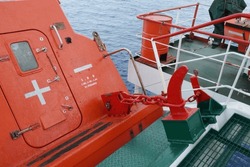 View on release mechanism of orange free fall lifeboat with hook and chain secured on launching ramp on stern part of vessel and ready for abandon ship with crew during emergency situation. 