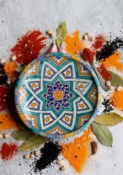 Oriental ceramic plate and different spices on a table. Light gray background. Beautiful decorative plate close up photo. 