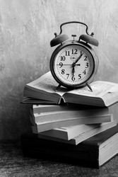 Still life with vintage mechanical alarm clock. Retro objects on grey background with copy space. Stack of old books close up photo. 