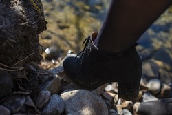a woman's leg in a dark stocking and black shoes steps on the rocks by the water