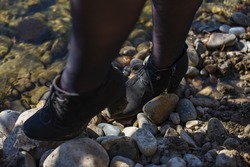 women's legs in dark stockings and black shoes step on the rocks by the water