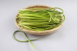 Close-up of raw green garlic scapes on bamboo basket on white background, South Korea   
