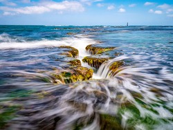 Long exposure view of wave and waterfall on sea rock with green laver with the background of sea horizon at Mopo-ri near Pohang-si, South Korea  
