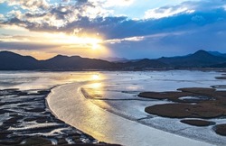Sunset and aerial view of curved sea waterway and mud flat at low tide against sunshine at Suncheon Bay near Suncheon-si, South Korea 
