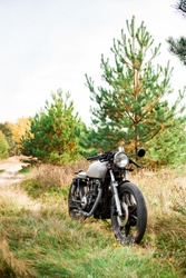 Silver caferacer motorcycle parking on a country road. Everything is ready for having fun driving the empty road on a motorcycle tour journey. Modern hipster hobby. Space for your individual text.