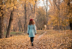 Back view of elegant young woman in gray casual coat in autumn. Cute model walks in the park in golden autumn against background of nature. Autumn walk.
