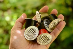 Hand holding coffee capsules used to be discarded with defocused foliage background.