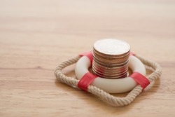 Stacked coins in red lifebuoy or lifebelt with wooden background copy space. Assets wealth, money saving or money investment protection and security by insurance concept. Risk management analysis.
