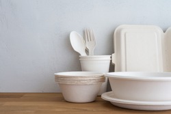 Natural eco-friendly disposable utensils (fork, spoon, dish plate, bowl, cup and fast food box container) made of fiber of bagasse and bamboo on wooden table with white wall background. Save the earth