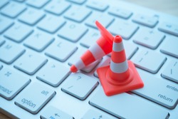 Maintenance, repair, under construction in computer system from virus or ransomware concept. Close up orange white traffic warning cones or pylon on keyboard computer background with copy space.