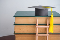 Graduation cap on textbooks with pencil ladder in classroom background copy space. Business education, abroad educational and goal or target successful graduation concept.