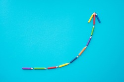 Flat lay of color pencils curve graph growth up form on blue background with copy space. Business growth, creative idea, kids art education and development concept.
