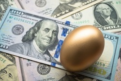 Bright golden egg on US dollar bill banknotes background. Rich, wealth, successful from stock dividend yield in stock market investment. Business, financial, investment and retirement planning concept