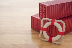 Lifebuoy with red containers on wooden table background with copy space. Marine cargo shipment or freight insurance in global shipping and logistic industry. Insurance is risk management control.
