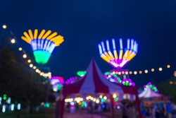 Blurred image of people in funfair amusement park festival in city park at night bokeh background. Summer festival holiday vacation concept.