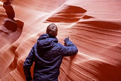 Man standing inside beautiful Antelope slot canyon, Page, Arizona. Guy with gloves and winter jacket hiking through narrow pathways in between smooth sand stone formations.