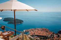 Umbrellas provide shade to the restaurant's diners on the top of the Srd hill overlooking the old town of Dubrovnik. Panoramic view of the city from the height of the mountain.