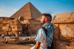 A tourist man stands with his back to the camera and looks at the pyramids. Meditation near the pyramids in Cairo, Egypt
