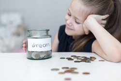 A little girl saves money for a dream. child counts and puts coins in a glass bottle in her room. The child saves money on the concept of the future