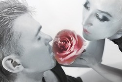 Studio portrait of young men and women with silver makeup on his face, sniffing a flower pink rose
