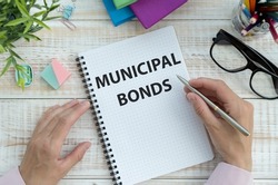 Businessman holding a card with text MUNICIPAL BONDS. Keyboard, diagram and white background.