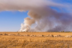 Autumn steppe. Dry yellow grass. Smoke over the steppe. Smoke from a fire in the steppe. Smoke screen over the plain. Smoke in the blue sky. Ecological problem. Rubbish. Environmental pollution