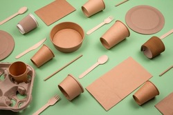Set of different eco-friendly tableware and kraft paper food packaging on green background. Street food paper packaging - cups, plates, straws, containers, paper bags and wooden cutlery. Mockup