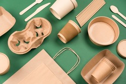 Eco-friendly tableware - kraft paper utensils on green background. Paper cups and containers, wooden cutlery. Street food paper packaging, recyclable paperware, zero waste packaging. Mockup, flat lay