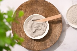 Bowl with gray cosmetic clay cream on wooden tray - mineral bentonite facial mask. Skincare beauty concept. Top view