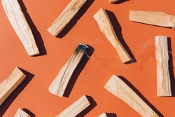 Burning incense - palo santo sticks over orange brown background, Earth tone. Flat lay composition with holy wood sticks for meditation and spiritual practices. Room fumigation ritual. Selective focus