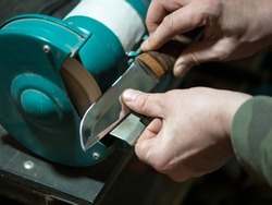 Knife sharpener and a hand with a blade, a man sharpens a knife on a grinder