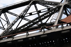 bottom up view of section of railway truss bridge against cloudy sky background