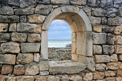 semicircular window opening in the ruins of an antique wall, behind which you can see the sea