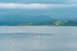 waterscape of the sea bay with a fishing ship and a foggy mountainous coast in the background, a view of the Mendeleev volcano from the side of the town of Yuzhno-Kurilsk