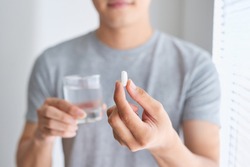 Happy asian man holding a pill and a glass of water looking at camera