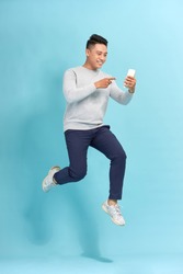 Full length of handsome  young man taking phone while jumping against blue background.