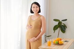 Beautiful pregnant woman standing near table with fresh vegetables