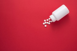 Pills spilling out of pill bottle and isolated on red. Top view with copy space. Medicine concept
