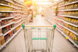 Supermarket aisle with empty red shopping cart with customer defocus background