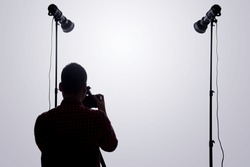 Professional photographer. Portrait of confident young man in shirt holding hand on camera while standing against grey background